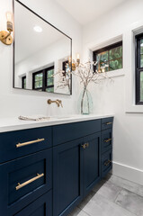 Beautiful bathroom in new luxury home. Features vanity with faucet, sink, mirror, cabinets, and sconce lights.