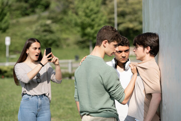 Two bullies menacing teenager boy and girl filming on phone. Cyber bullying and violence concept. - obrazy, fototapety, plakaty