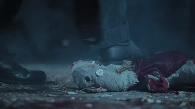 Close-up shot of a man crushing down a teddy bear. Man stepping or walking on a teddy bear in dramatic light.

