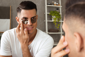 Man applying dark under eye patches near mirror at home