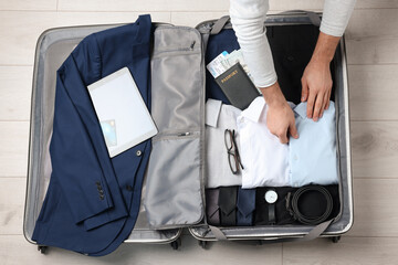 Man packing suitcase for business trip on wooden floor, top view