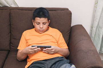 child lying in the chocolate chair looking at the cell phone