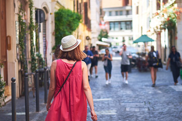 Woman walking on street. Woman tourist in red dress with hat walking on street of Rome on sunny day.