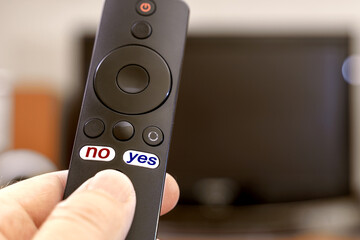 TV remote in hand with yes and no button labels. The inscription No in red and the inscription Yes in blue on the buttons of the TV remote control
