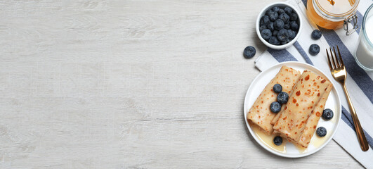 Delicious crepes served with blueberries, honey and milk on white wooden table, flat lay with space for text. Banner design