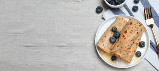 Delicious crepes with blueberries and honey on white wooden table, flat lay with space for text. Banner design
