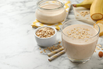 Glass of tasty banana smoothie with oatmeal on white marble table. Space for text