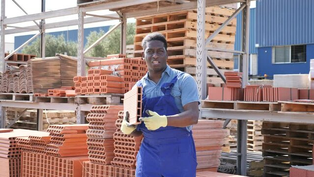 African-american man carrying hollow concrete blocks in outdoor construction material warehouse. High quality 4k footage
