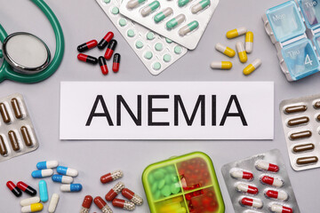 Card with word Anemia, stethoscope and different pills on white background, flat lay