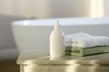 Fototapeta na wymiar Bottle of bubble bath and towels on white table in bathroom, space for text