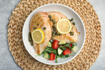 Delicious cooked chicken fillets with capers and salad on light grey table, top view