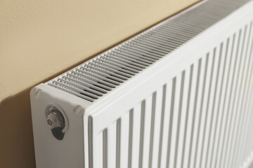 Modern radiator on beige wall, closeup. Central heating system