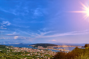 Croatian coastal landscape with wide blue sky where sun is shining and small town in front of island in foreground