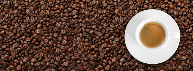 Cup of tasty aromatic coffee on roasted beans, top view. Banner design