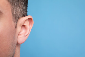 Man on light blue background, closeup of ear. Space for text