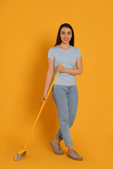 Beautiful young woman with broom on yellow background