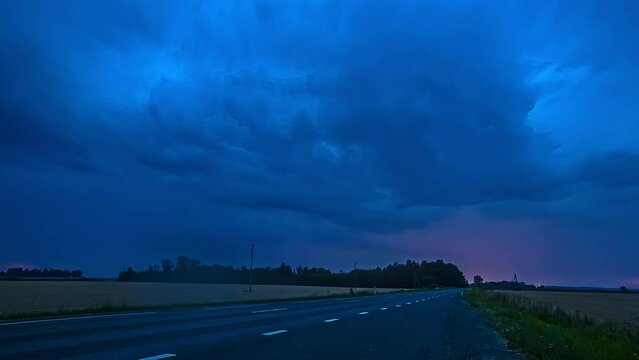 Low angle shot of lightning of dark storm clouds over a busy highway with cars passing by in timelapse.