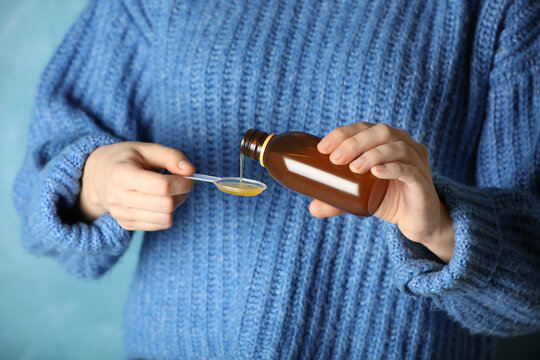 Woman pouring cough syrup into spoon on light blue background, closeup