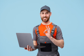 Handsome smiling delivery man in uniform with laptop looking at camera and showing okey sign