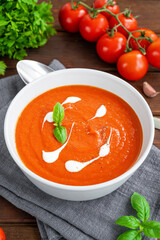 Tomato soup puree in a bowl with cream and fresh basil leaves on a dark wooden background. Copy space. Top view.