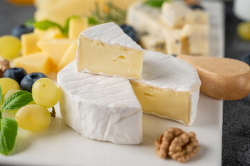 Cheese plate with a variety of cheeses, honey, grapes, nuts, olives, blueberries and fresh herbs on a concrete background. A festive snack.