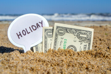 Paper bills one dollar and small stick with paper speech bubble with word Holiday buried in sand...