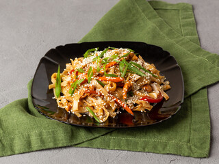 Asian vegetarian food udon noodles with mushrooms, sesame and pepper close-up on a black plate