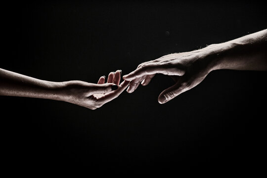 Romantic touch with fingers, love. Two hands stretch each other, black background. Couple in love holding hads, close up. Helping hand, support, friendship. Tenderness, tendet touch.
