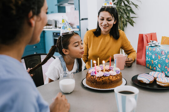 Young daughter blows out the candles, celebrating a happy birthday at home with her two moms 
