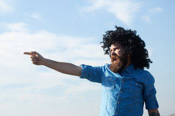 Crazy funny bearded man with black wig pointing finger on sky background. Funny facial expressions.