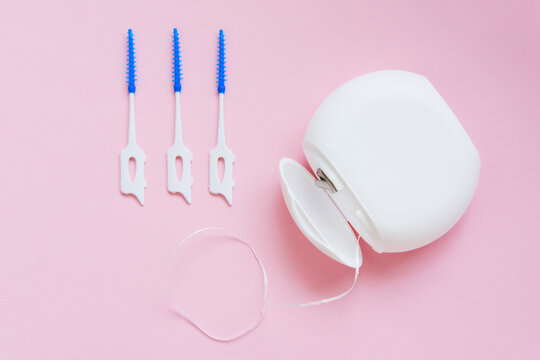 Oral Care: Dental Floss and brush for cleaning interdental spaces on a pink background. Top view. Concept: dental services, oral hygiene, dental care.