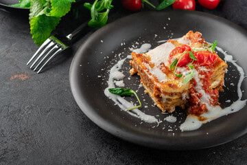A portion of meat lasagna with bolognese sauce and mozzarella cheese on a black plate. Italian dish with layers of pasta and minced beef, copy space