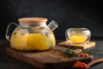 Autumn sea buckthorn tea with orange in a glass teapot and cups with fresh berries and cinnamon. Hot Vitamin drink with steam