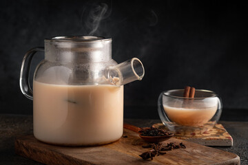 Masala tea with milk in a teapot with a steaming mug. Indian chai with spices and milk