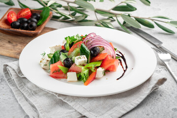 Greek salad is the national dish of Greece with tomatoes, cucumbers, red pepper, olives, feta cheese and lettuce leaves seasoned with olive oil. Served on a white table