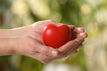 Fototapeta na wymiar Elderly woman holding red heart in hands on blurred green background, closeup