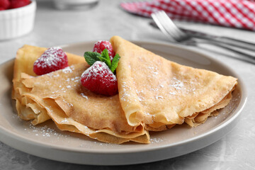 Delicious crepes served with mint, raspberries and powdered sugar on grey table, closeup