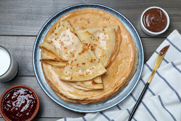 Delicious crepes served with chocolate paste, jam and milk on wooden table, flat lay