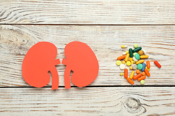 Paper cutout of kidneys and pills on white wooden table, flat lay