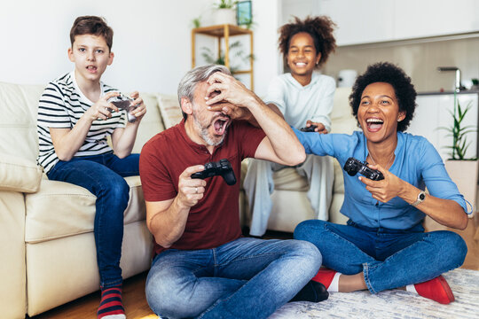 Smiling family enjoying time together at home sitting on sofa in living room and playing video games.
