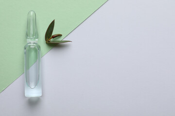 Pharmaceutical ampoule and green leaves on color background, flat lay. Space for text