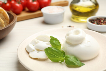 Delicious burrata cheese with basil served on white wooden table, closeup