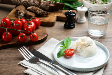 Delicious burrata cheese with basil and cut tomato served on wooden table
