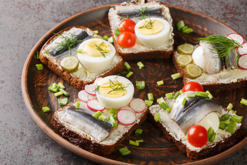 Rye bread toasts with butter, sprat fillet, eggs, various vegetables close-up in a plate on the table. horizontal