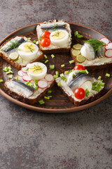 Sandwich with sprat fillet, eggs, various vegetables close-up in a plate on the table. Vertical