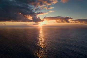 Aerial view of setting sun in dramatic clouds over Atlantic ocean.