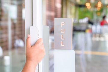 Closeup woman's hand going to pull the swing door to enter the cafe, open glass door with matal...