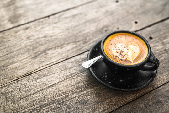 Cappuccino coffee in black ceramic cup on old wood plank table