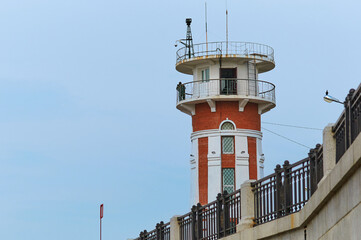 Lighthouse on the embankment against the blue sky without clouds. Border guard silhouette.