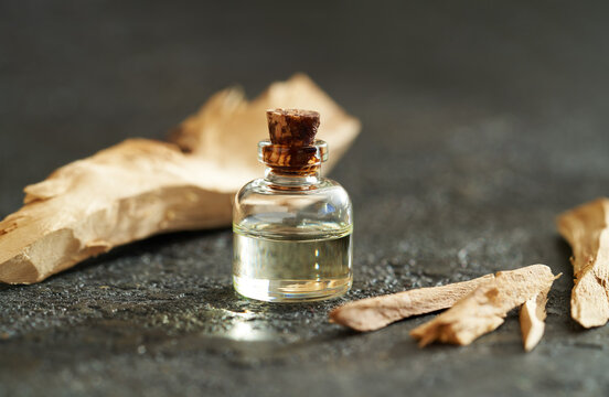 A bottle of sandalwood essential oil with white sandalwood on dark background